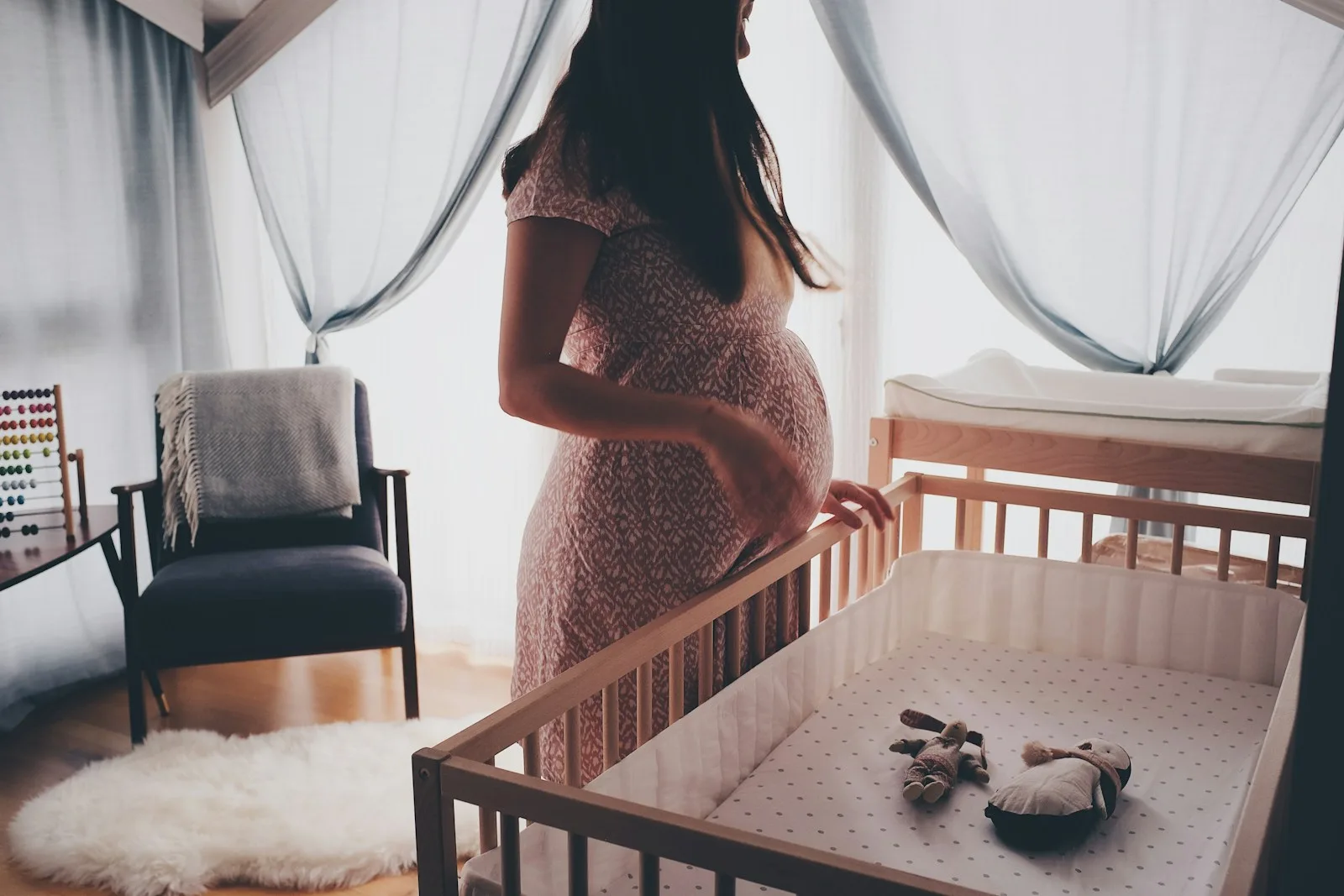 An expectant mother beside a cot in a softly lit nursery